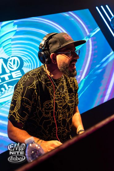 DJ performing energetically at Emo Nite Dubai event with vibrant background visuals.