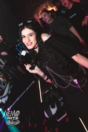 Young woman holding a camera, smiling at a night event in Dubai.