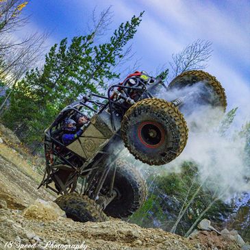 Off-road vehicle performing a wheelie on rugged terrain with smoke around.