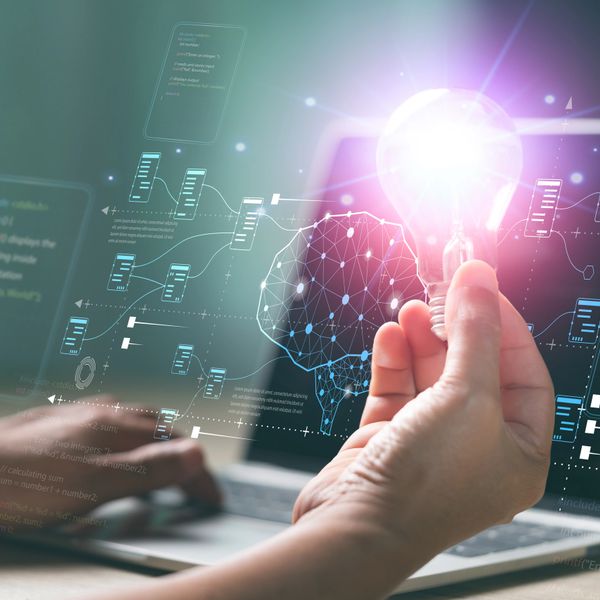 Hand holding glowing light bulb with digital brain and code overlay.
