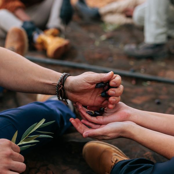 Two people exchanging small berries and a leaf while sitting on the ground.