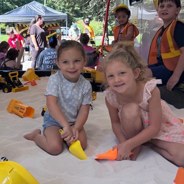 Two young girls playing in sand with toy construction tools.