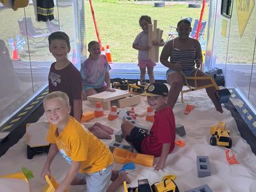 Kids playing in a sandpit with toy construction vehicles.