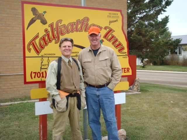 Two men posing in front of a Tailfeather Inn sign.