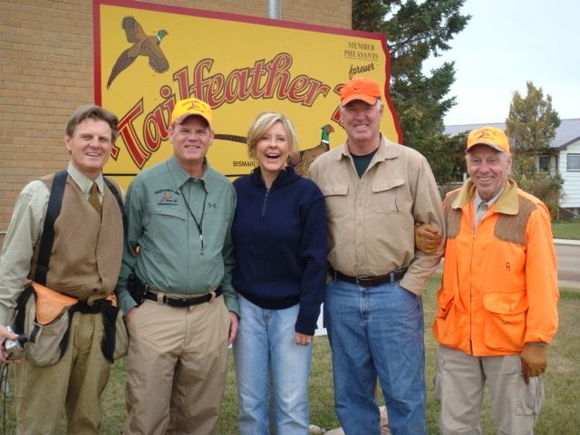 Five people posing in front of a Tailfeather sign.