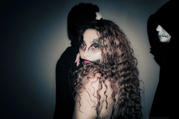 Woman with spooky makeup and long curly hair looking at the camera.