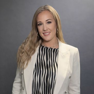 Smiling woman in white blazer and striped blouse against gray background.