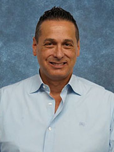 Man in a light blue shirt smiling against a blue textured background.