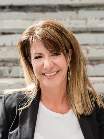 A smiling woman with shoulder-length hair wearing a black blazer.