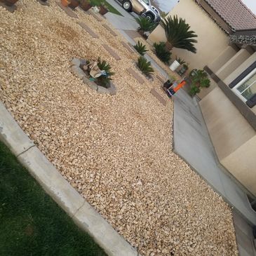 Jardín delantero con piedras decorativas y plantas.