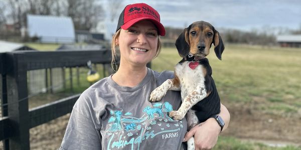 Woman holding a small dog outdoors, smiling at the camera.