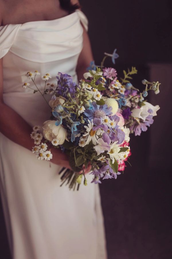 Bride in white dress holding colorful bouquet.