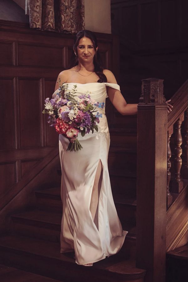 Bride in white dress holding a colorful bouquet on stairs.