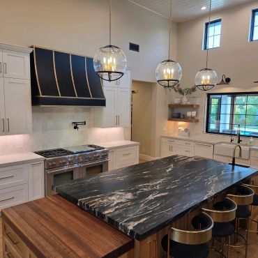 Modern kitchen with a large black marble island and brass-accented stools.