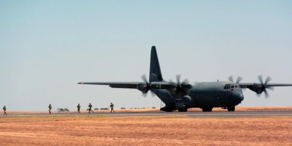 Military plane taxiing with soldiers nearby.