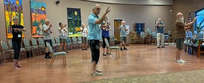 Group of seniors practicing Tai Chi in a spacious room with colorful wall art.