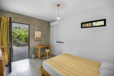 Ljust sovrum med minimalistisk inredning och vy mot en hammock utomhus.