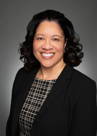 Professional woman smiling in a black blazer with checkered top.