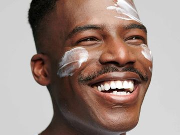 Client smiling with moisturizer applied to face, enjoying a moment of self-care and radiant skin.