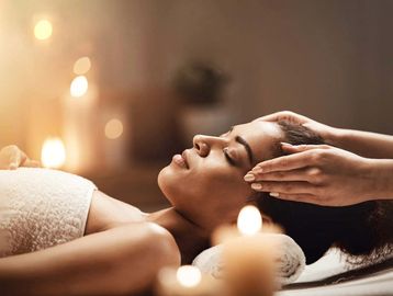 Woman getting facial in candlelit spa, surrounded by a serene & luxurious ambiance.