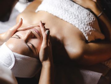 Woman in white wrap & headband getting relaxing facial massage, enjoying serene spa experience.
