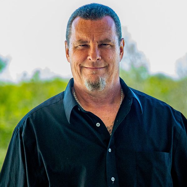 Smiling man in a black shirt outdoors with a natural background.