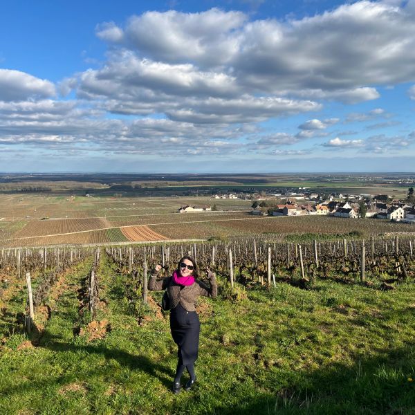 Woman posing joyfully in a vineyard under a partly cloudy sky.