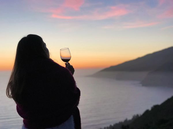 Woman enjoying wine at sunset by the ocean.
