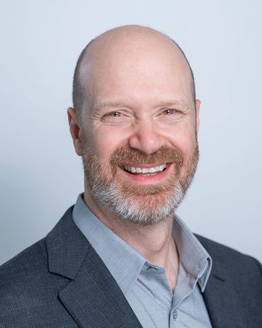 A smiling bald man with a beard in a gray suit.