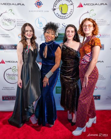Four women in elegant dresses posing on a red carpet.