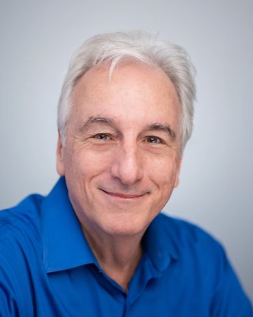 Smiling man with white hair in a blue shirt.