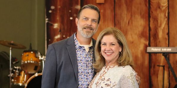 A smiling couple posing indoors with musical instruments in the background.