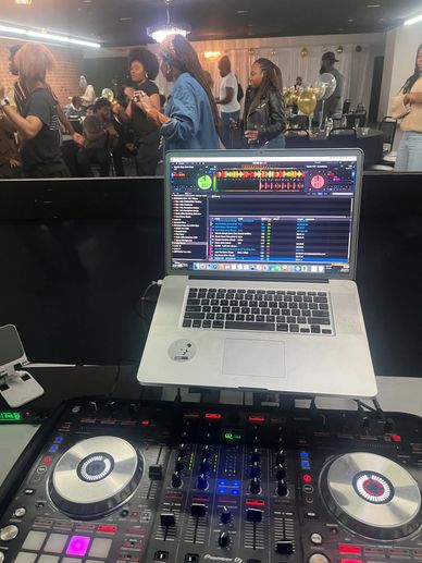 DJ setup with laptop and mixer at a lively indoor party with people dancing.