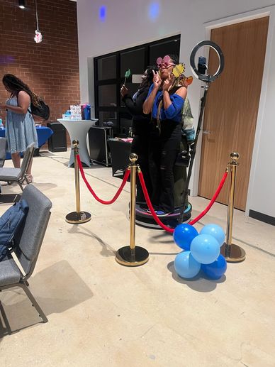 Women posing behind a red rope barrier with balloons.