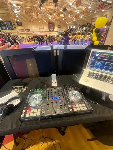 DJ setup in a gymnasium with a dance performance and audience.