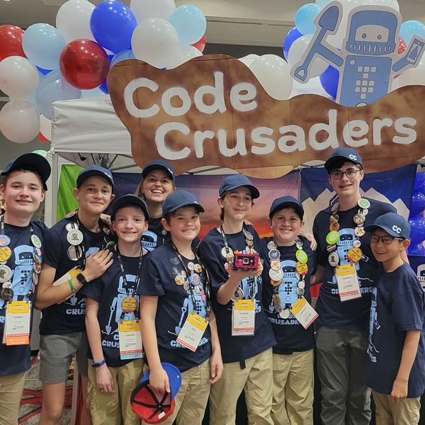A group of kids and a mentor wearing matching Code Crusaders shirts and badges.