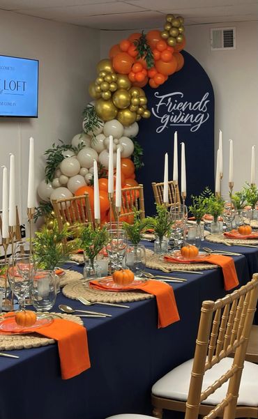 Elegant Friendsgiving table with pumpkins, candles, and colorful balloons.