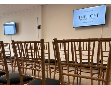 Rows of empty chairs face two screens in a room labeled 'The Loft'.