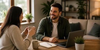 Two people having a friendly conversation over coffee at a table with a laptop.