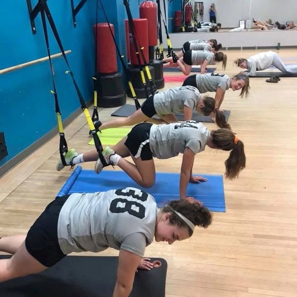 Group fitness class doing plank exercises on mats with TRX straps.