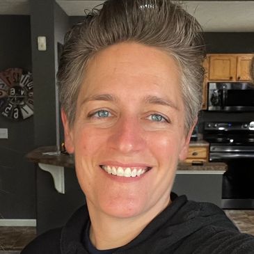 Smiling person with short gray hair in a kitchen.