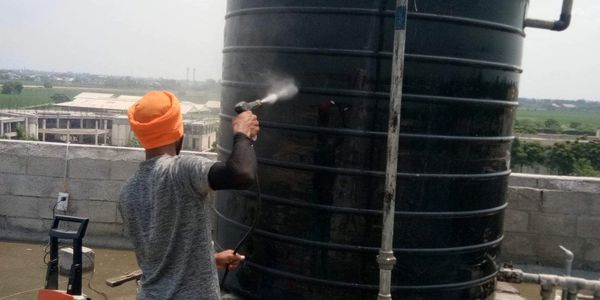 Two men cleaning a large black water tank on a rooftop.