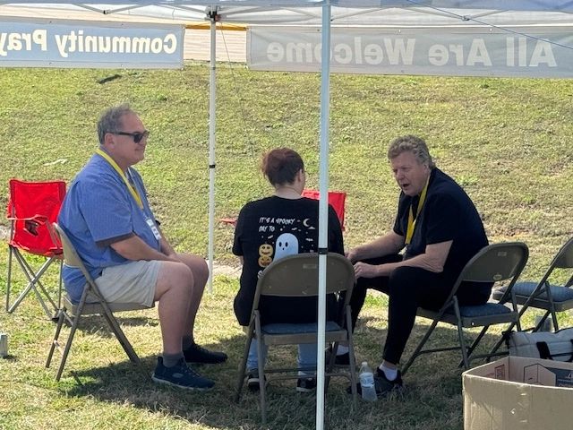 Three people sitting under a tent in a community event setting.