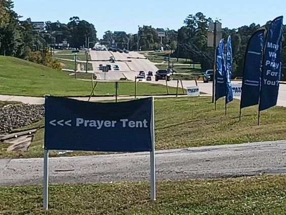 Sign pointing to a prayer tent near a road with flags.