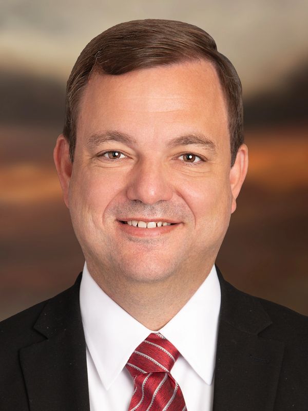 Professional man in a suit with a red tie smiling against a blurred background.