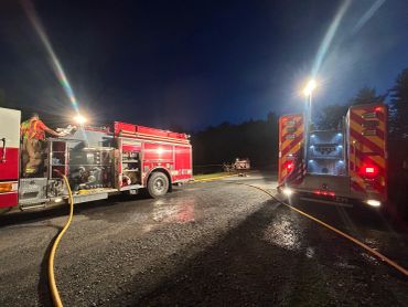 Two fire trucks with hoses deployed at night under streetlights.
