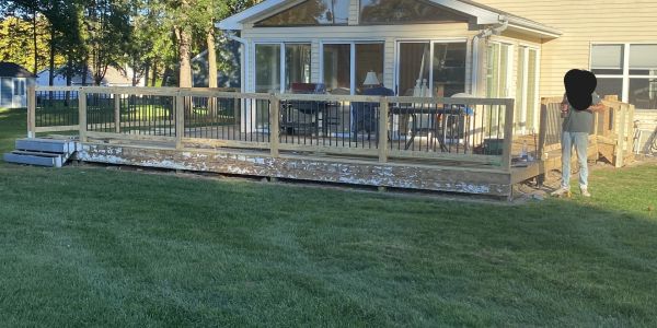 A beige house with a large wooden deck and green lawn in the backyard.