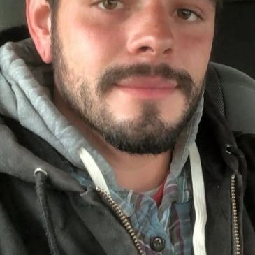 Young man with a beard wearing a hoodie and plaid shirt.
