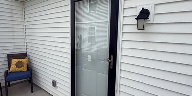 White exterior door with black trim and a chair with a sunflower pillow.