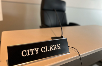 PICTURE OF EMPTY DESK WITH NAME PLATE STATING CITY CLERK